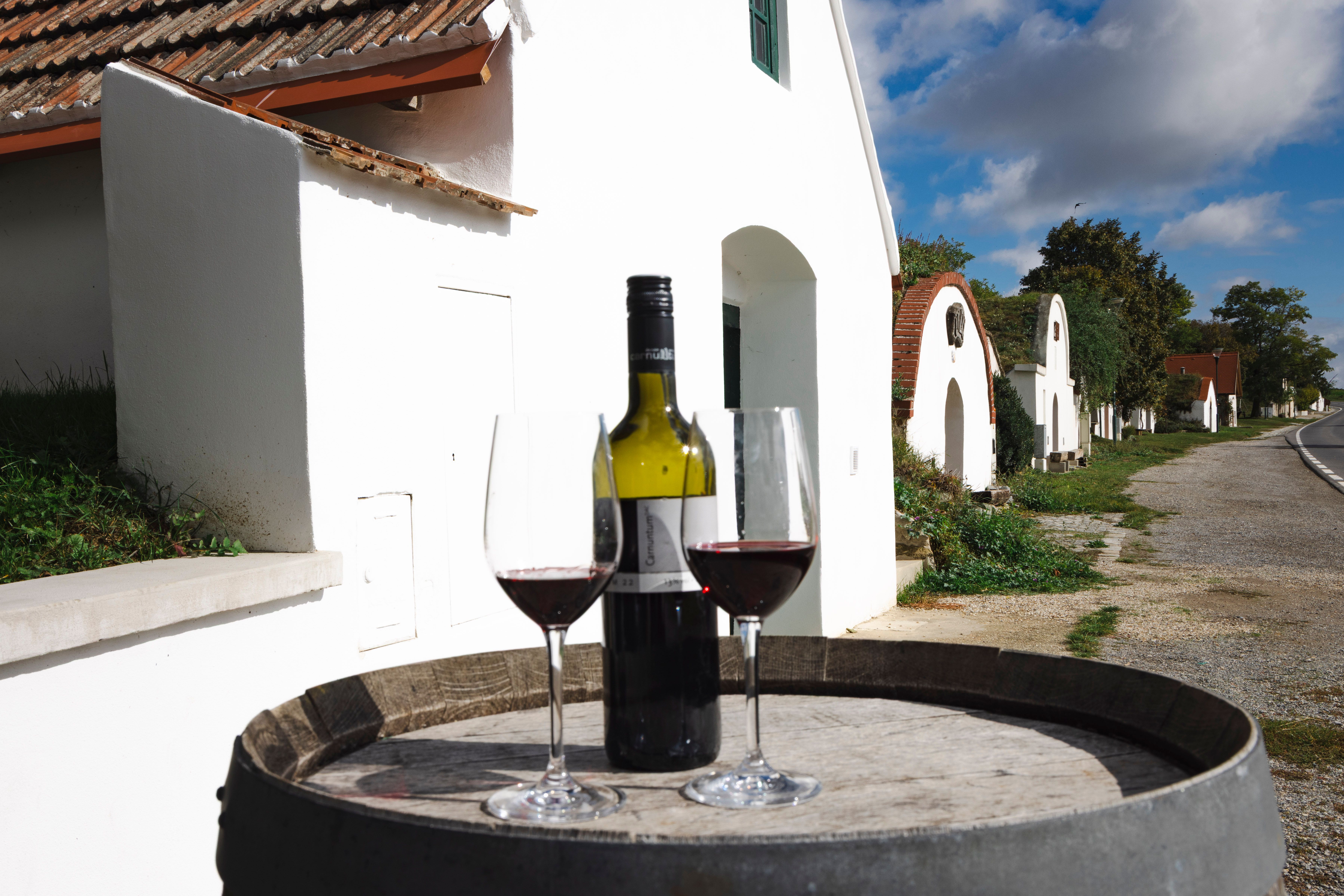 two wine glasses and a red wine bottle on a wine barrel, the wine cellar lane in the background