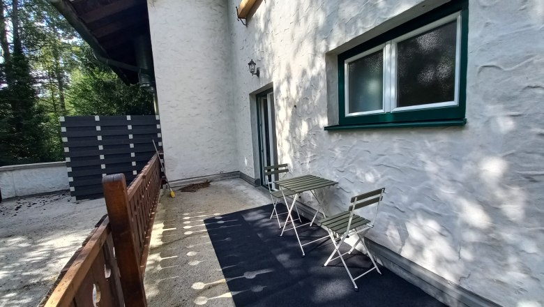Terrace of a vacation apartment with table and chairs, surrounded by trees.