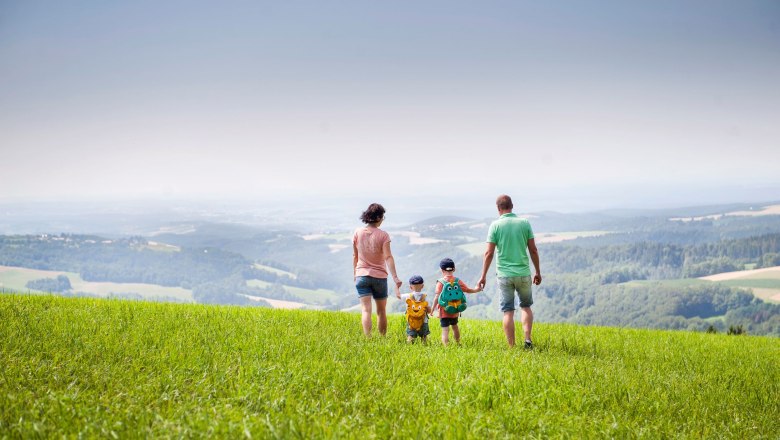 Family walks across a green meadow with a wide view of the countryside.