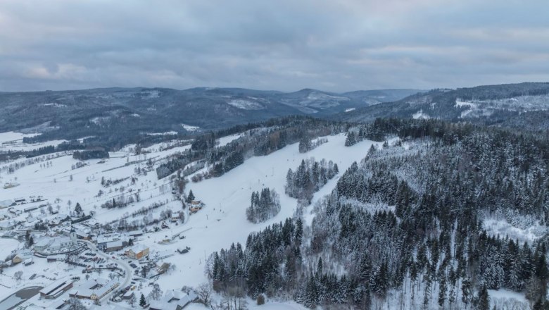 Aerial view of a snow-covered landscape with hills and forests.