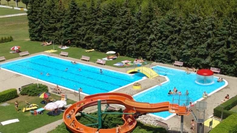 Aerial view of an outdoor pool with slide, two pools and sunbathing area.