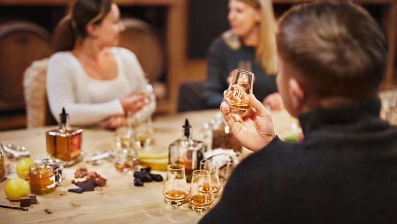 People at a whisky tasting at a table with glasses and ingredients.