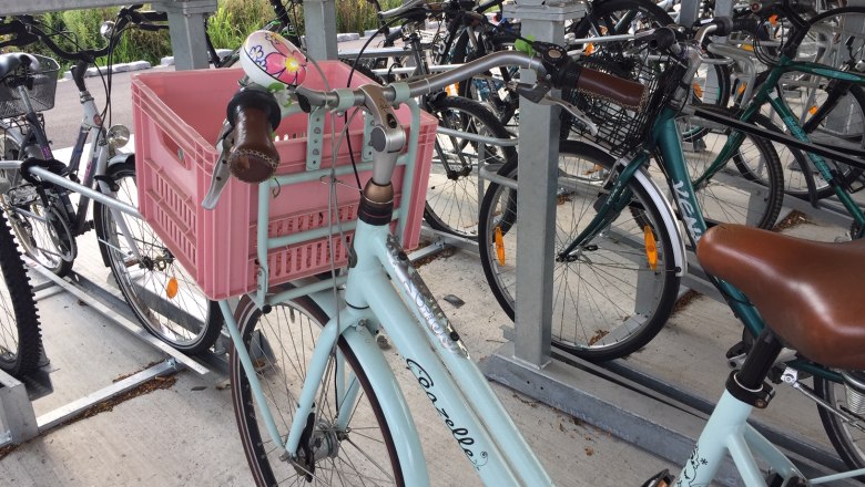 Bicycle with pink crate in a bicycle stand.