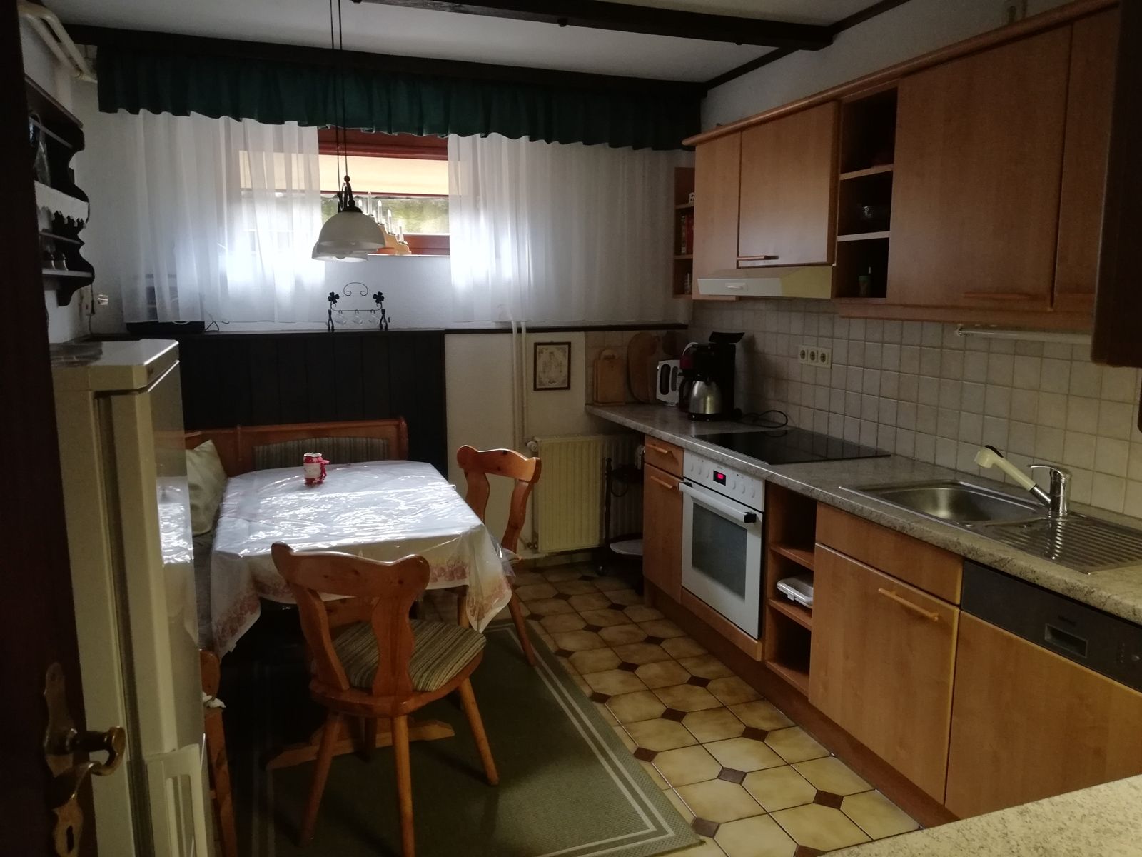 Cozy kitchen with wooden furniture, dining table, chairs and kitchen utensils.