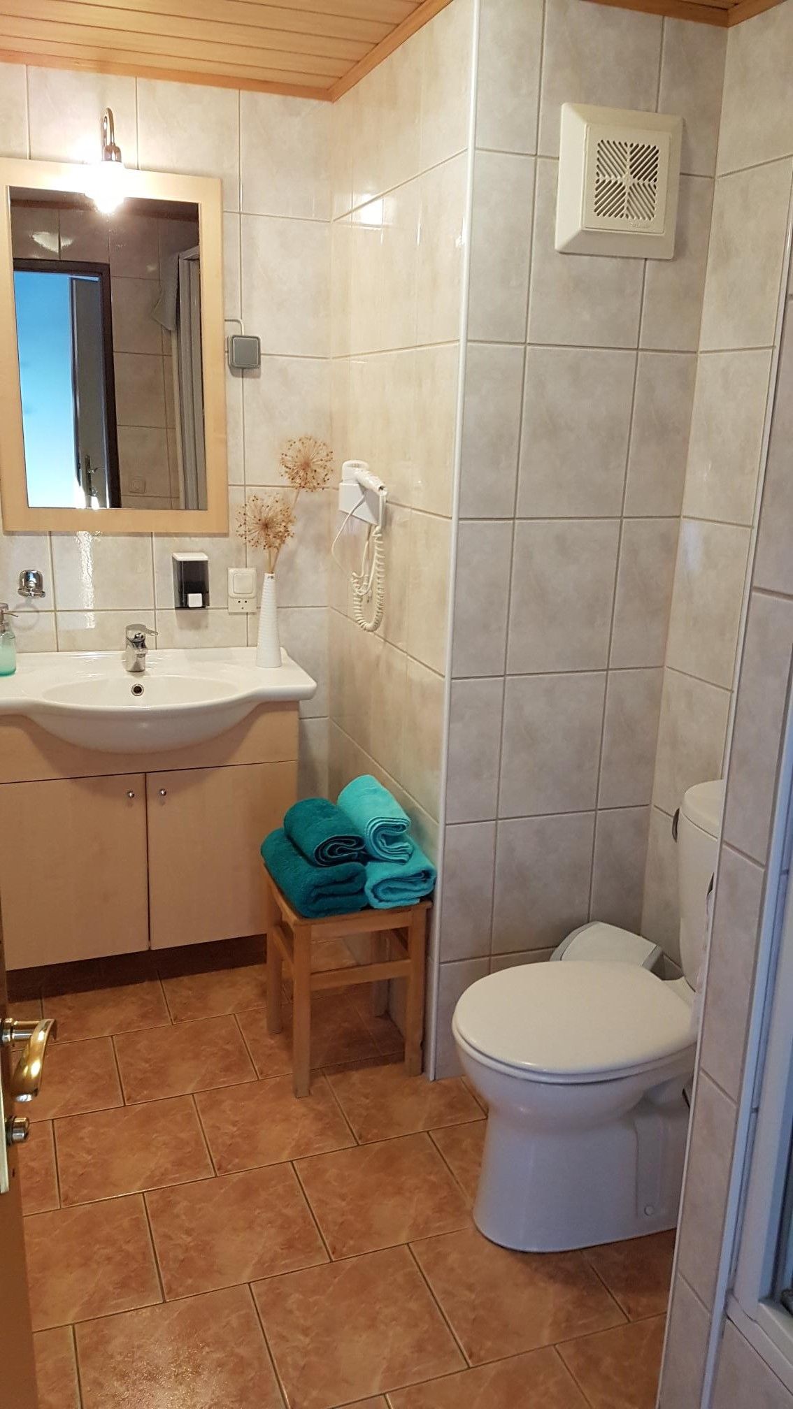 A bathroom with washbasin, mirror, toilet and towels on a stool.