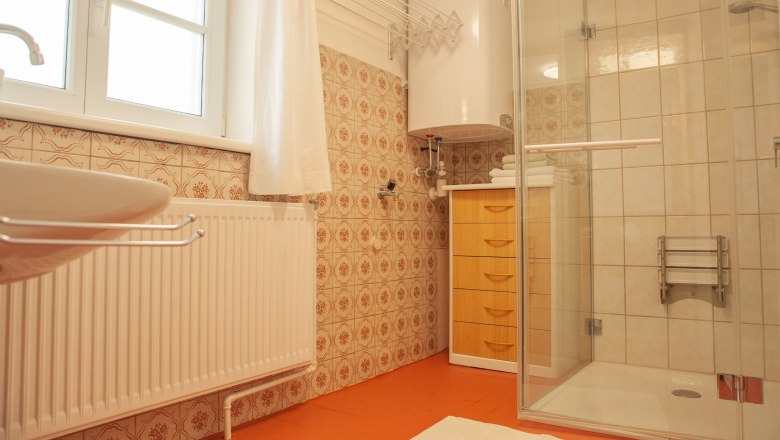 A bathroom with shower, washbasin, radiator and wooden cabinet. The walls are clad with patterned tiles.