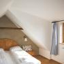 Cozy bedroom with sloping ceiling, double bed, wooden details and window with curtain.