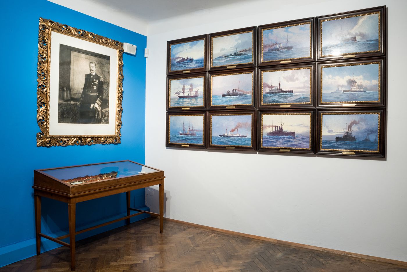 A museum room with maritime paintings and a portrait on the wall.