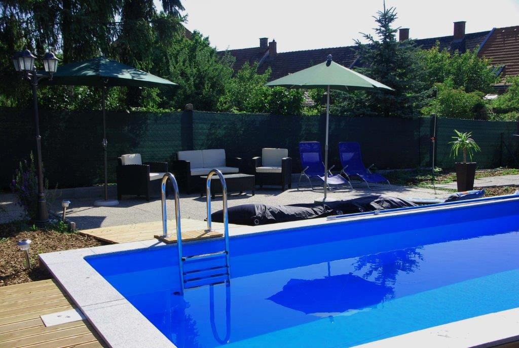 An outdoor area with a blue pool surrounded by sun loungers, parasols and garden furniture.