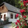A white house with a brown roof and red roses in the foreground.