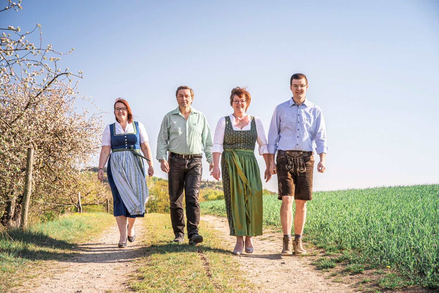 Four people in traditional dress walk along a country lane.