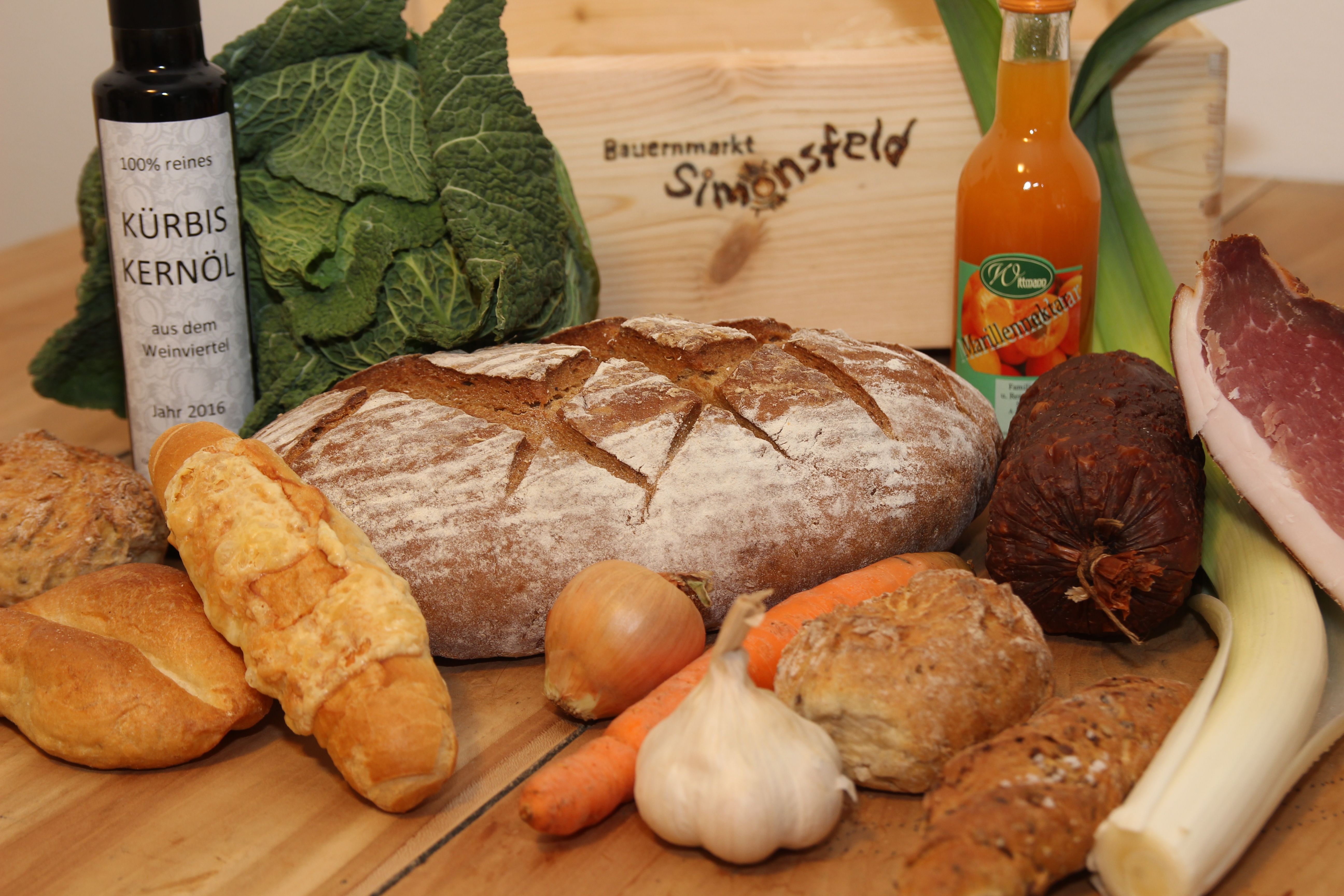 Various foods such as bread, vegetables, oil and sausage on a table.