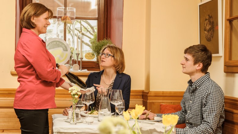 A waitress serves wine to a man and a woman in a restaurant.