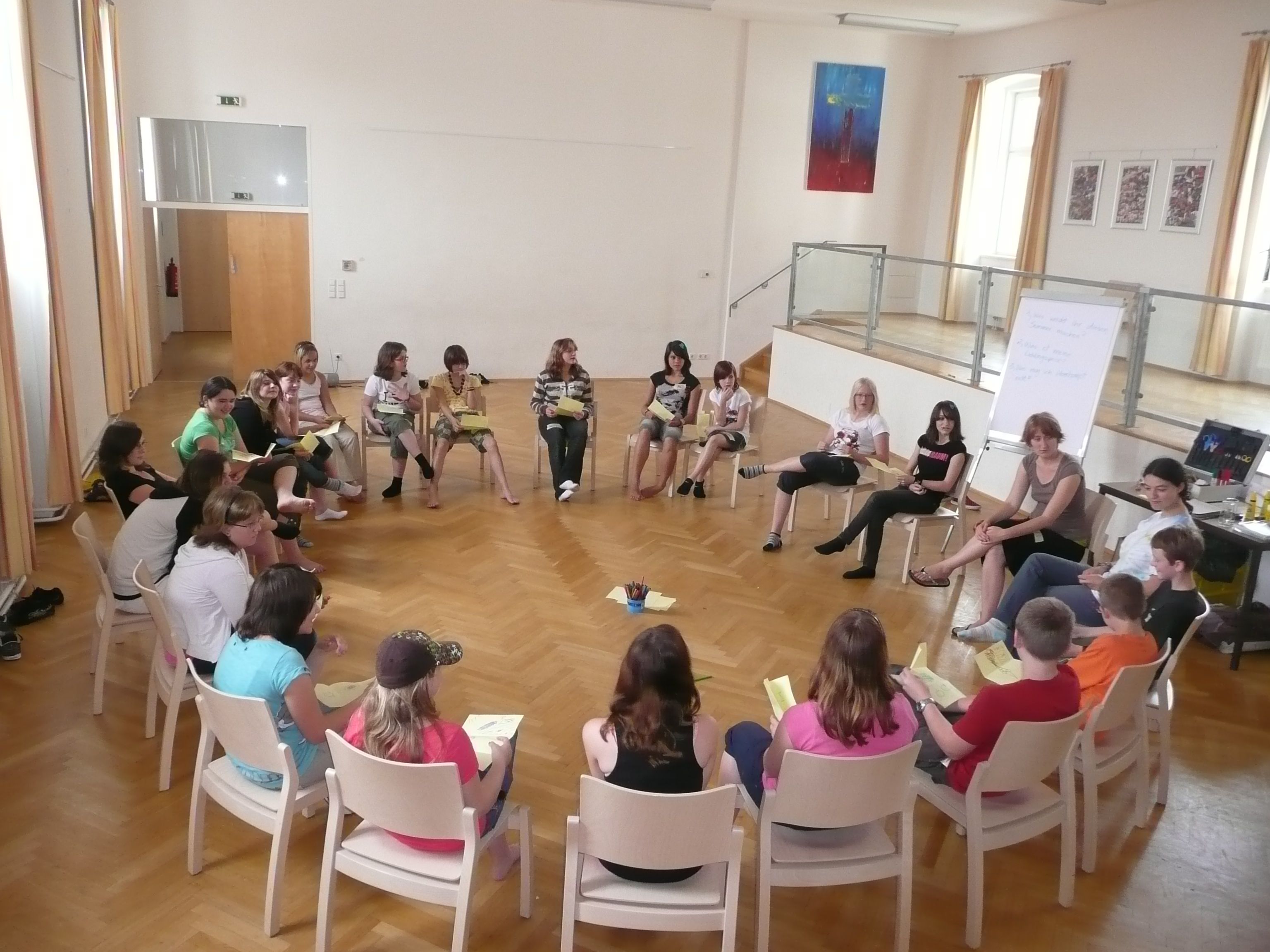 People sit in a circle of chairs in a large room.