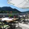 A guest garden with tables and chairs under parasols, with a view of the Danube and wooded hills in the background.