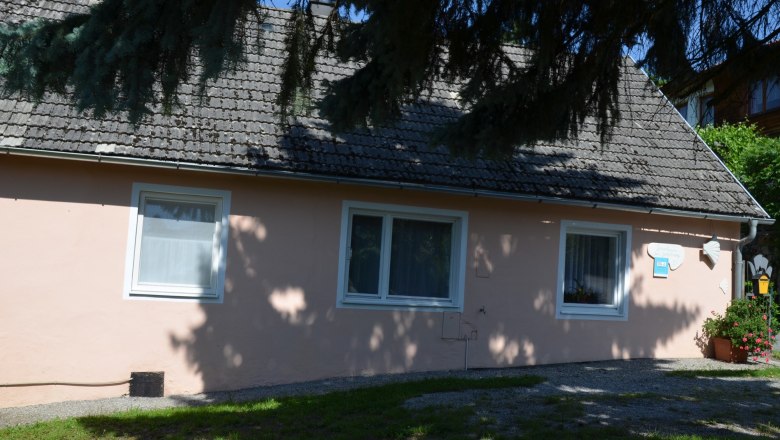 A small, pink vacation home with shady trees in the foreground.