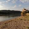 Pebble beach on the Danube with castle in the background at sunset.