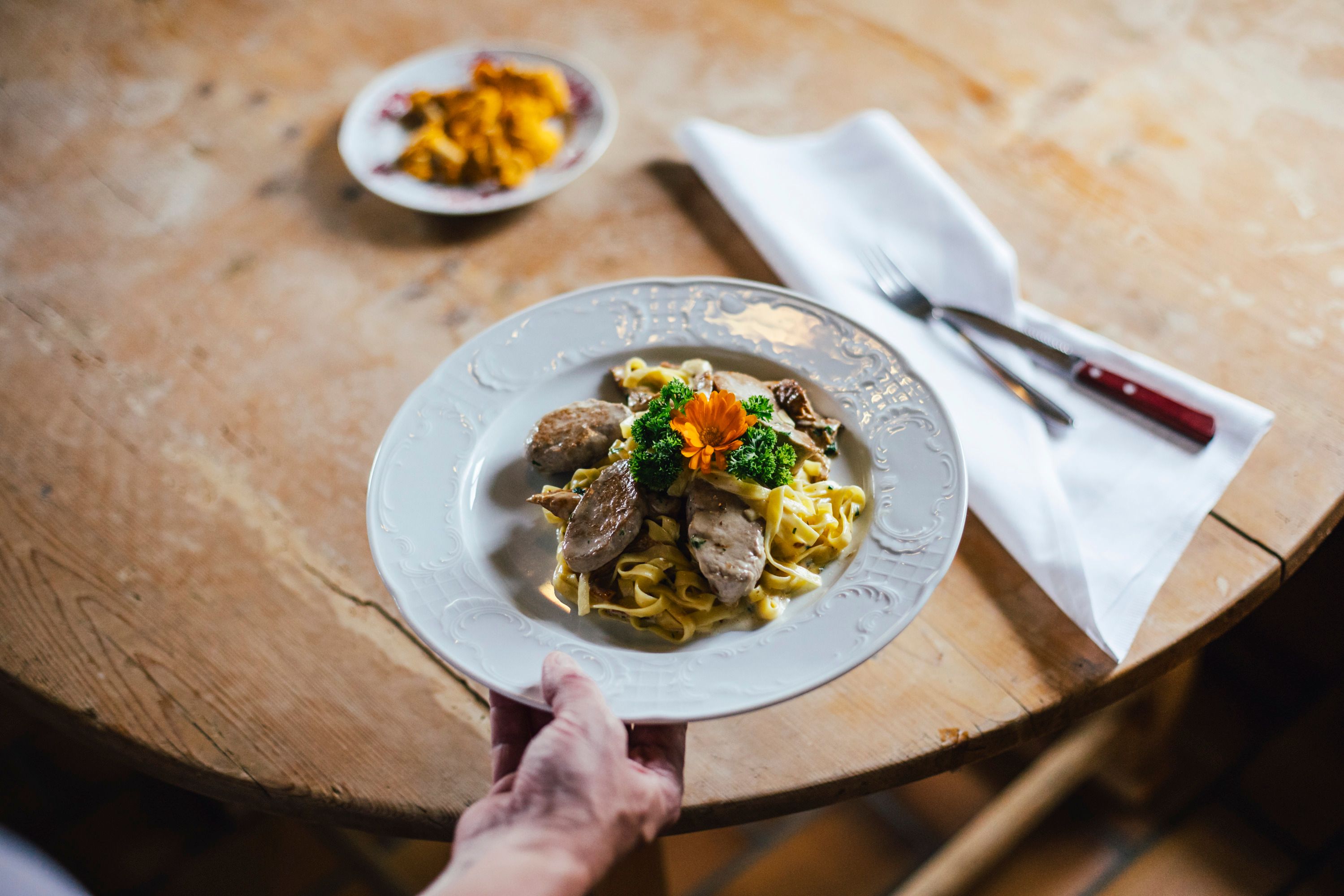 A plate of pork fillet tips and creamy chanterelle noodles on a wooden table.
