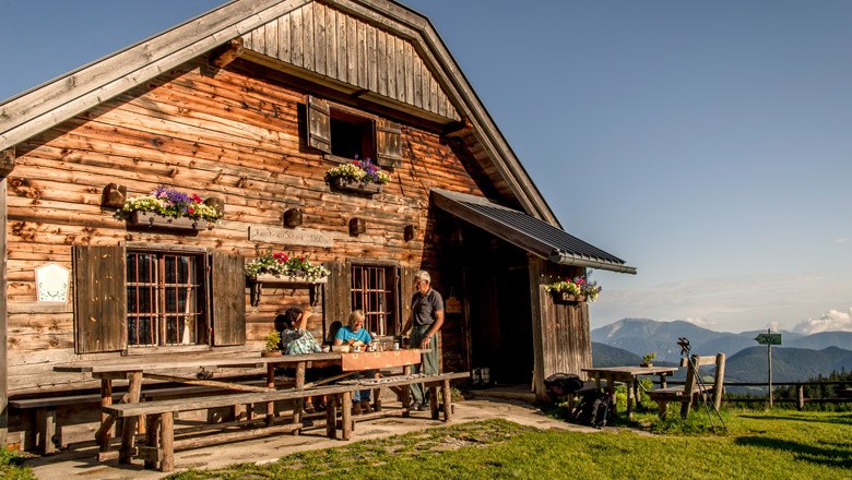 Wooden hut in the mountains with people at the table, blue sky.