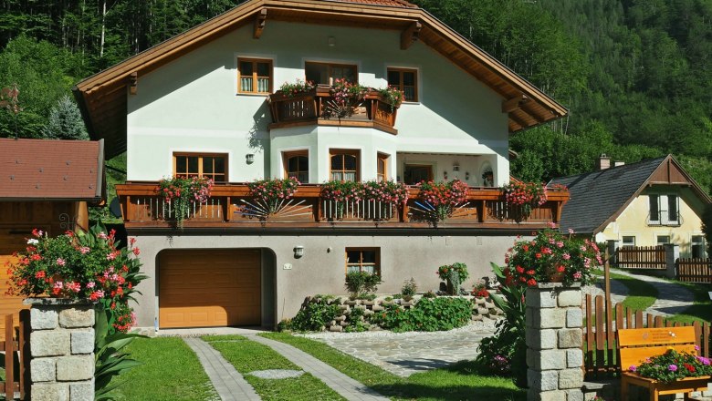 Private room Auer, © Roman Reichl A two-storey house with wooden balconies and flowers, surrounded by green countryside.
