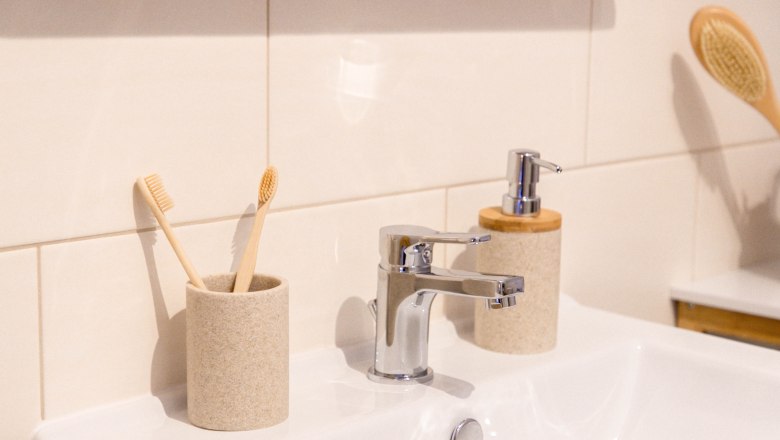 Close-up of a washbasin with two toothbrushes in a cup, a soap dispenser and a brush in the background.