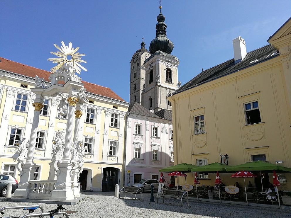 Historic square with baroque column, church and café.
