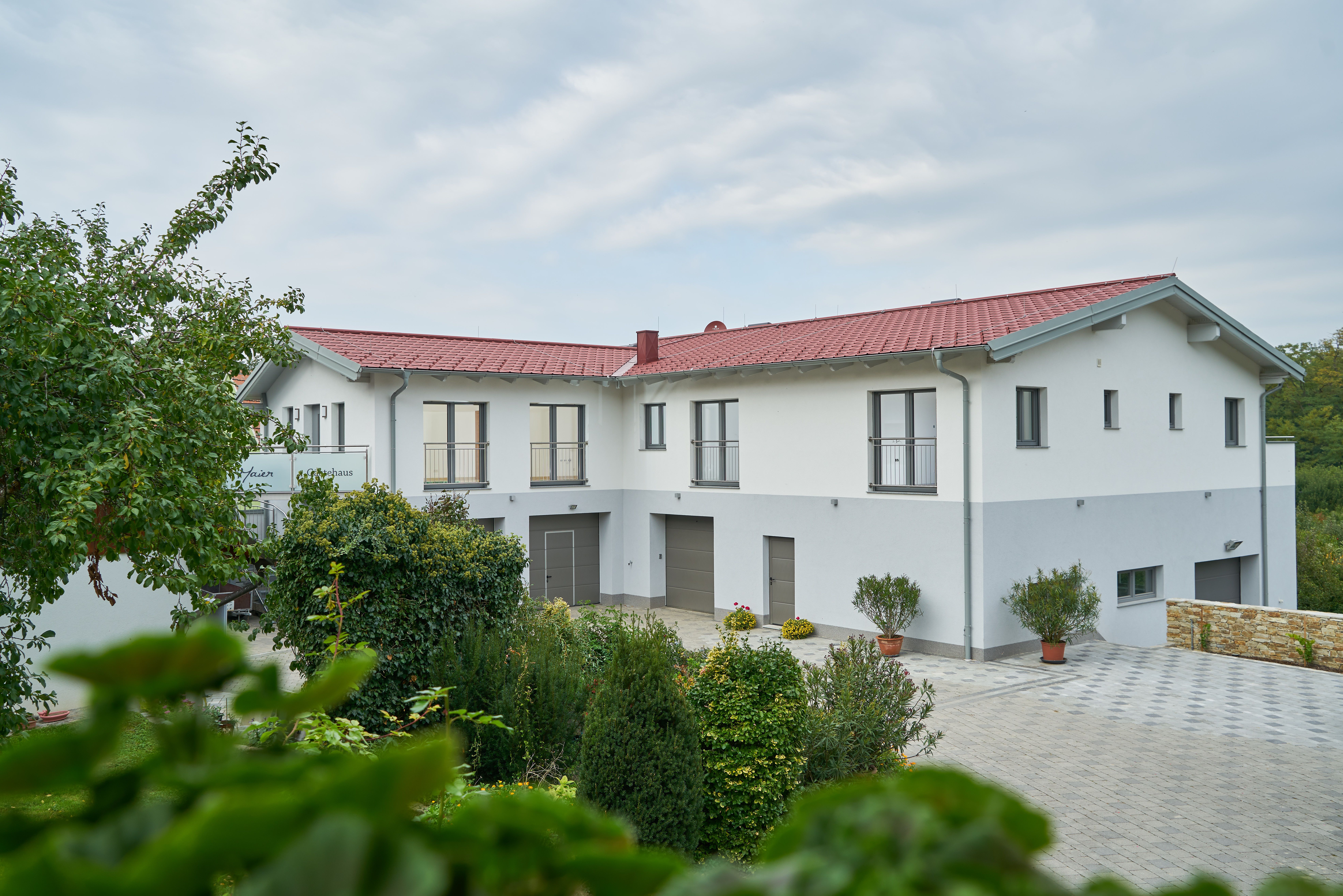 A modern building with a red roof and white walls, surrounded by green trees and plants.