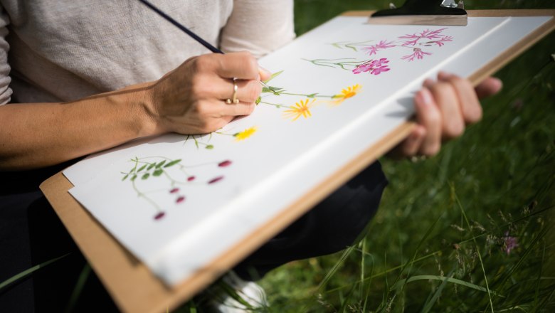 A person paints flowers on a clipboard outdoors.