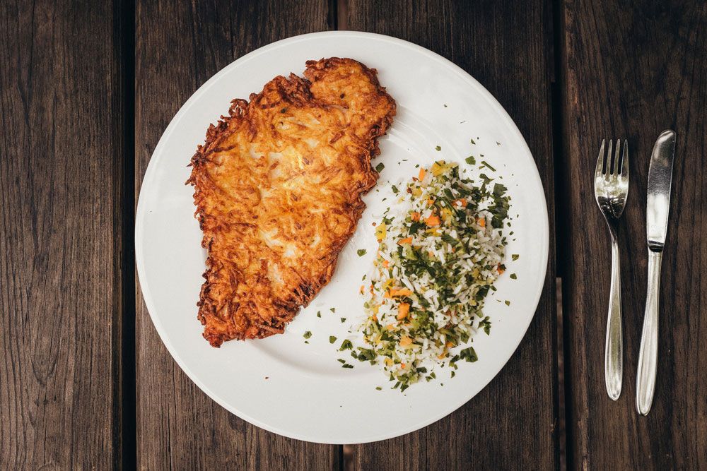 A plate with a potato cutlet and rice vegetables on a wooden table.