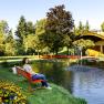 Woman sitting on a red bench by the pond in the spa gardens of Bad Sch&ouml;nau with trees and pavilion in the background.