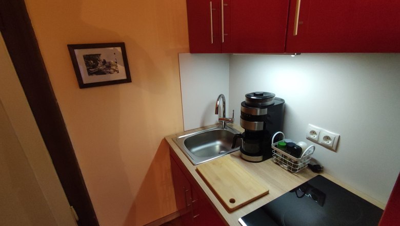 Small kitchen with red cupboard, sink, coffee machine and hob.