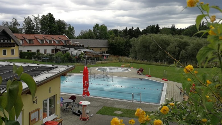 An outdoor swimming pool, surrounded by buildings and trees, under a cloudy sky.