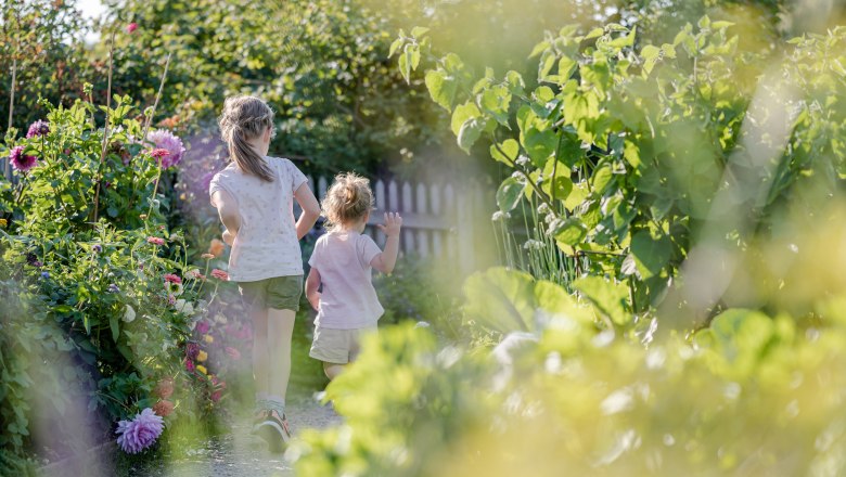 Two children run through a flowering garden path.