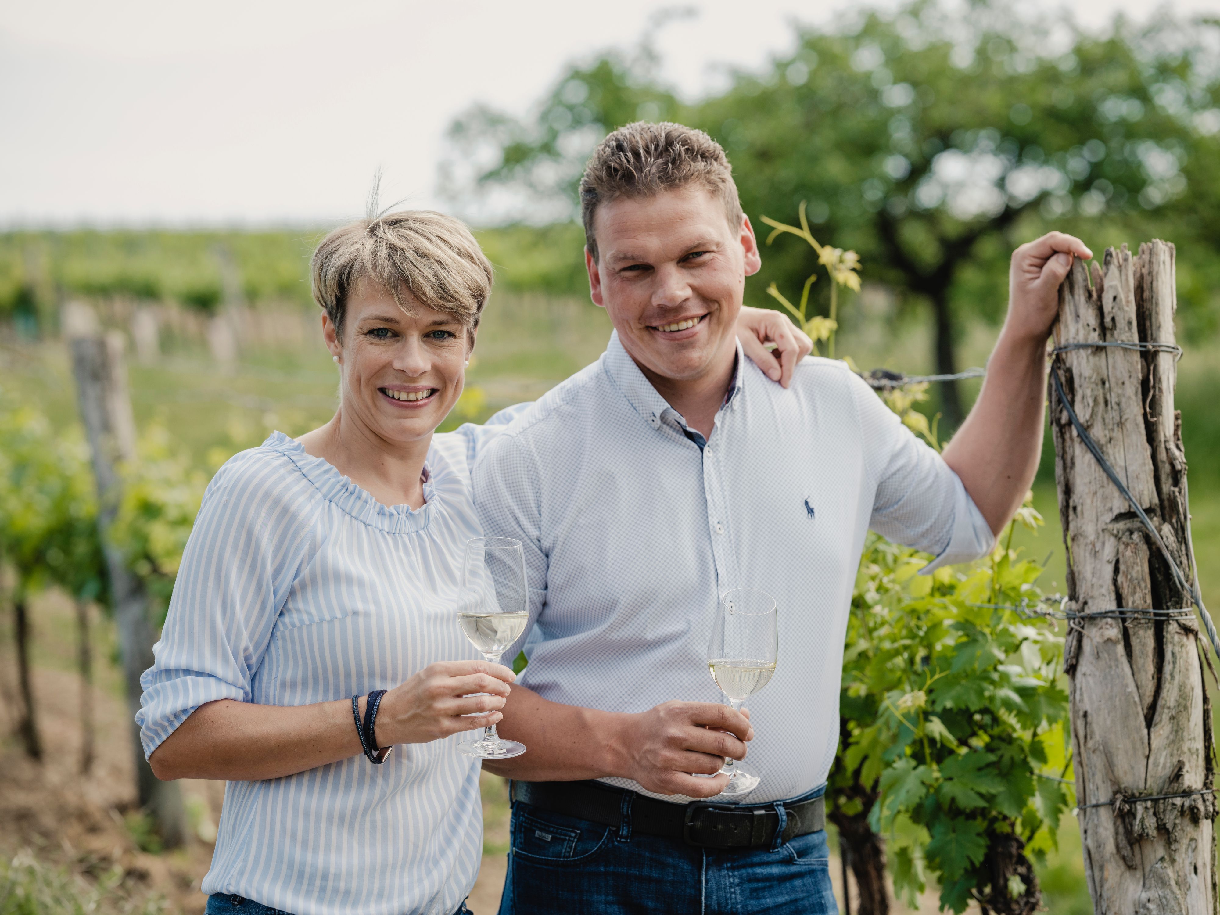 Two people in a vineyard with wine glasses.