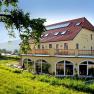 Yellow building with red roof and terrace, surrounded by green landscape.