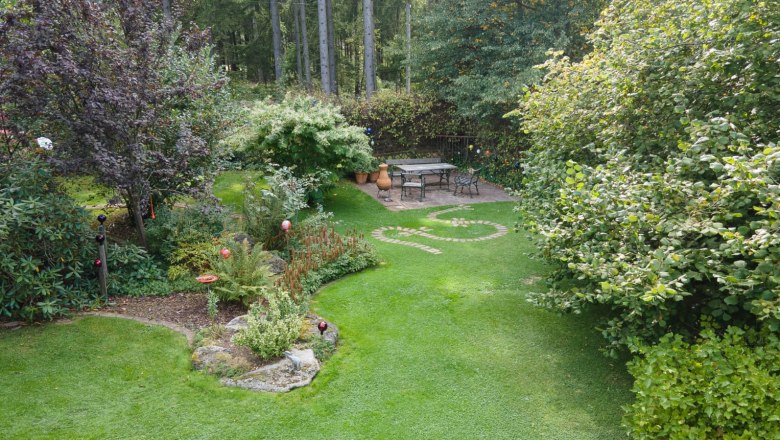 A well-kept garden with lawn, trees and a seating area on a terrace.