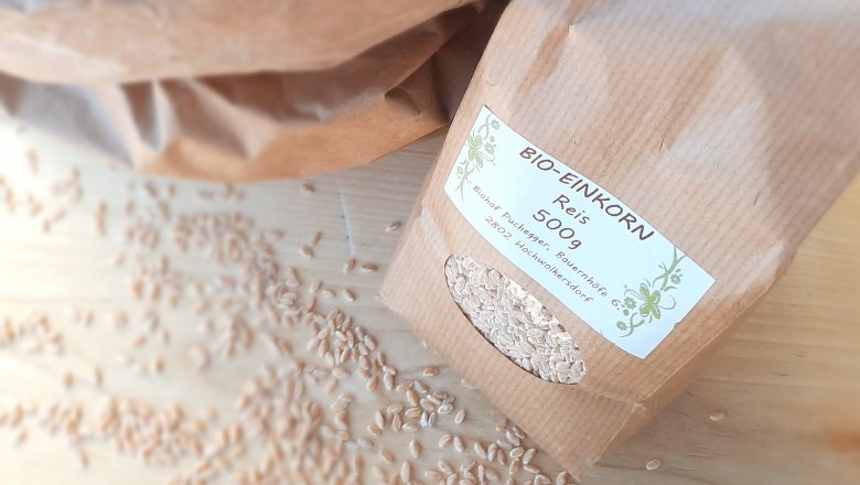 A packet of organic single grain rice on a wooden table surrounded by grains of rice.