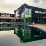 Modern wellness hotel with wooden façade and large pond in the foreground.