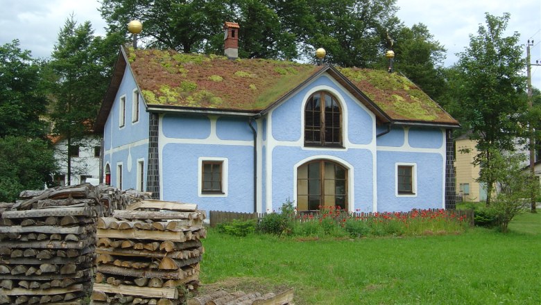 Blue house with grass roof and piles of wood in the foreground.