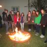 Group of young people standing around an outdoor fireplace.