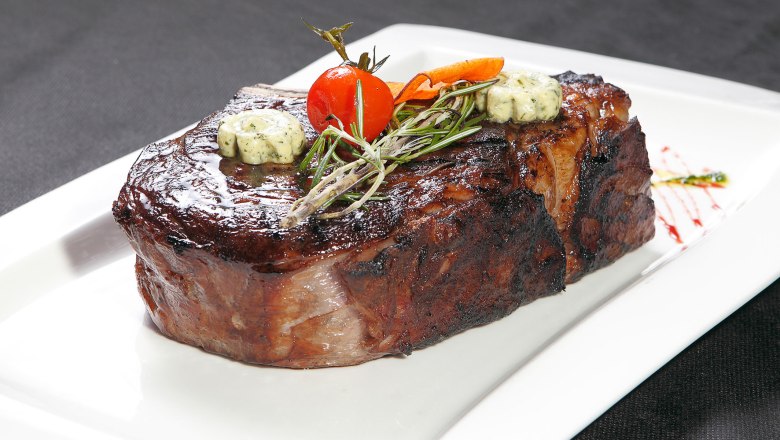 A juicy steak with herb butter, rosemary and a cherry tomato on a white plate.