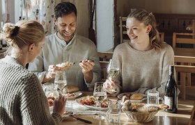 Three people sit at a table in a cozy restaurant and enjoy wine and food.