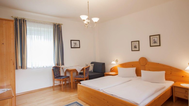 A cozy hotel room with a double bed, wooden furniture and a small table with chairs.