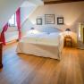 A cozy double room with wooden floor, a large bed, red curtains and stylish decorations.