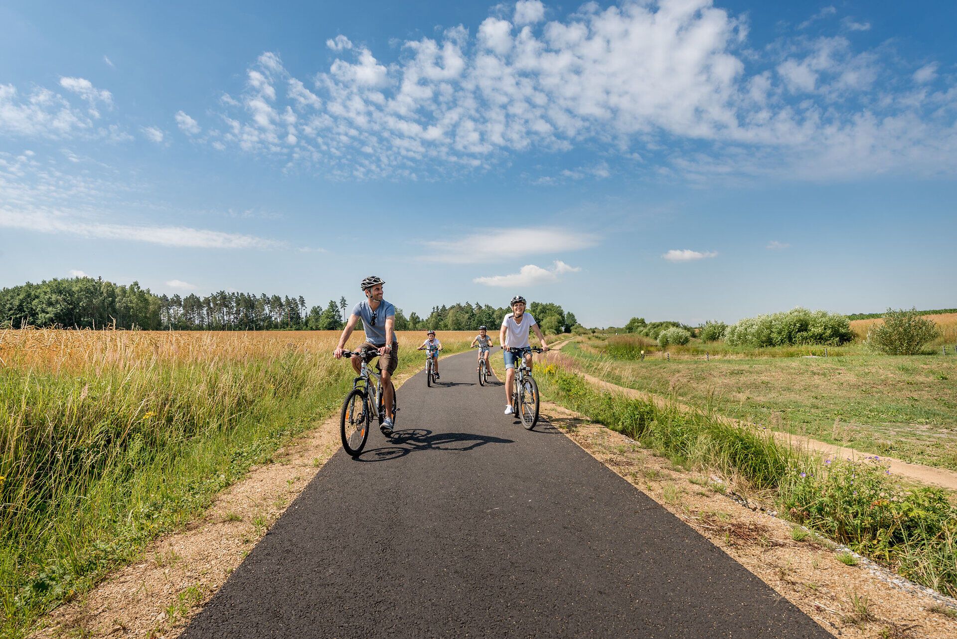 A family enjoys the fresh air and picturesque landscape during a bike ride. Surrounded by golden fields and rolling hills, summer radiates an inviting warmth that invites you to linger.