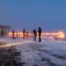 People standing on a snow-covered mountain terrace in the fog, illuminated by warm lights at dusk.
