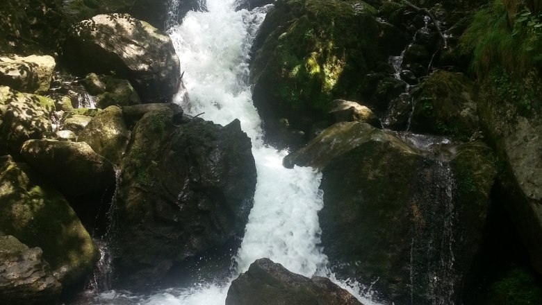 A waterfall flows over rocks in a wooded area.