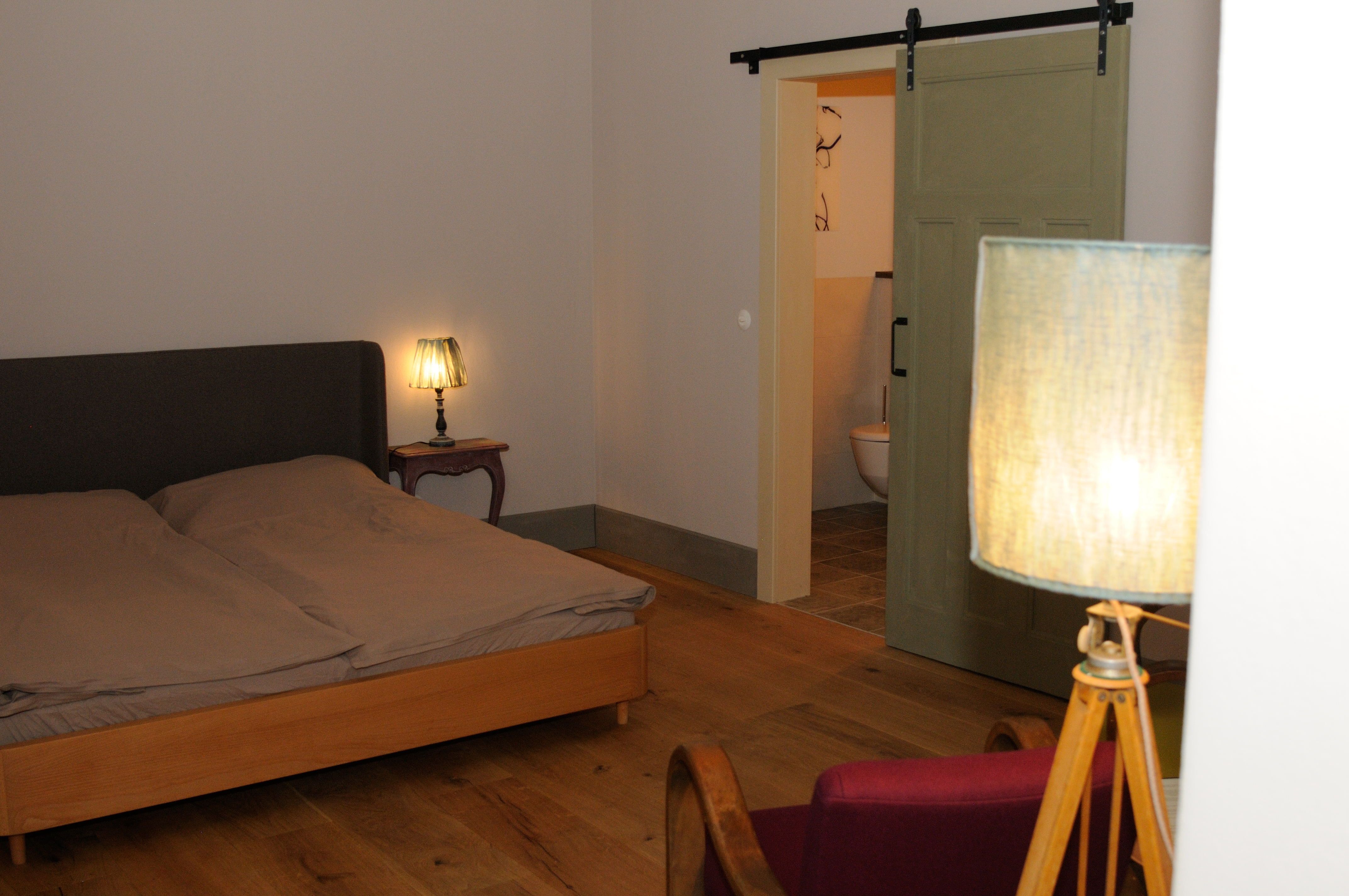 A cozy bedroom with double bed, bedside lamp and sliding door to the bathroom.