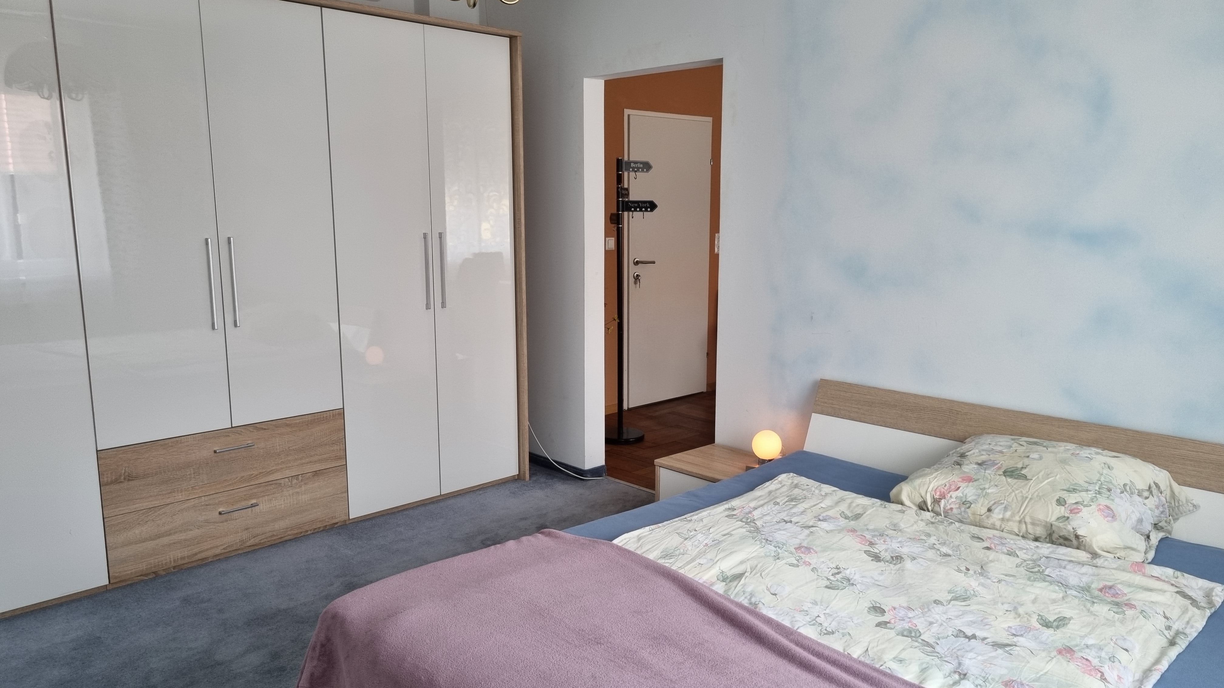 A bedroom with a double bed, a large white closet and a bedside lamp.