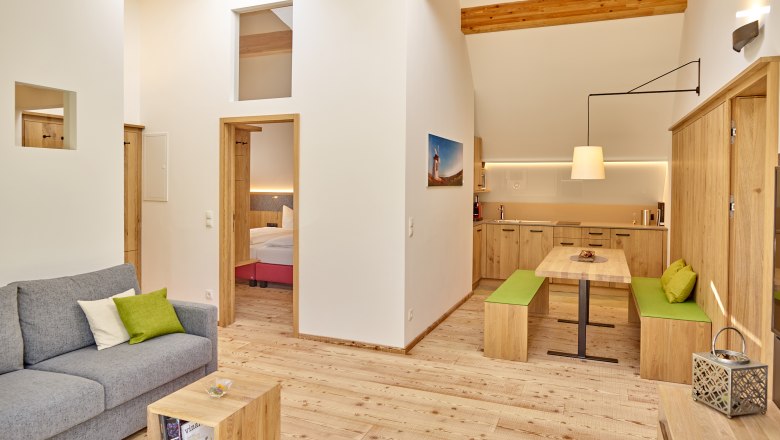 Modern living room with wooden furniture, gray sofa and open kitchen.